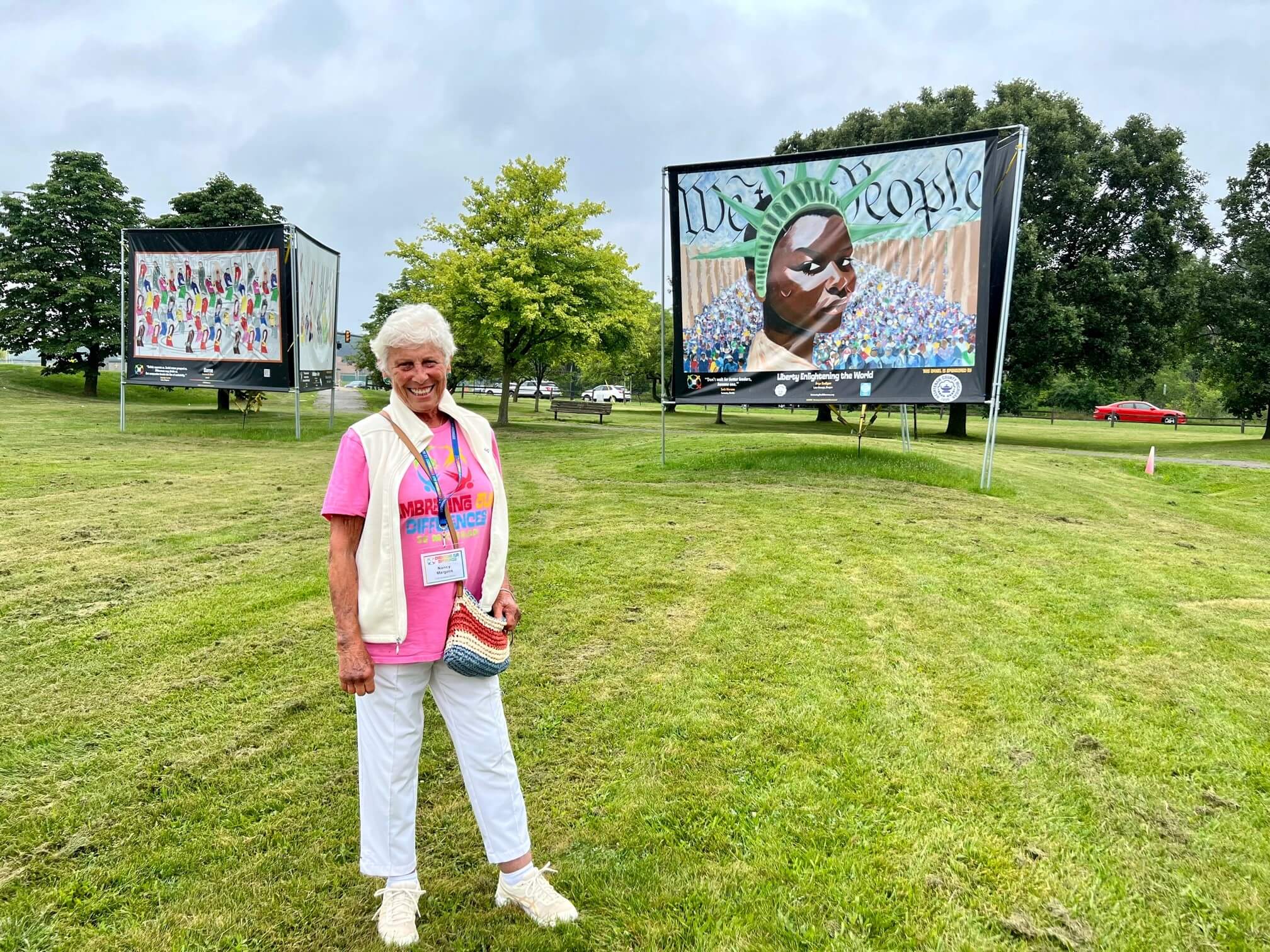 Nancy Margolis pictured at the Gallup Park installation with two signs of paintings behind her